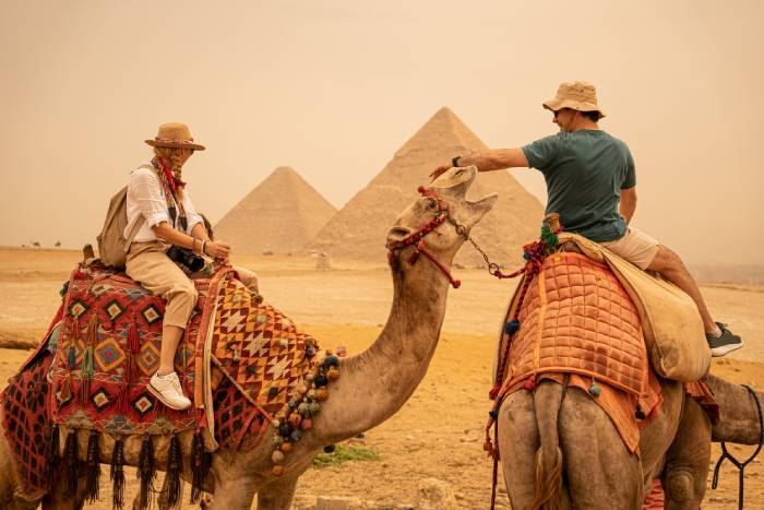 Tourists riding camels with the Great Pyramids of Giza in the background during an unforgettable desert adventure in Egypt.
