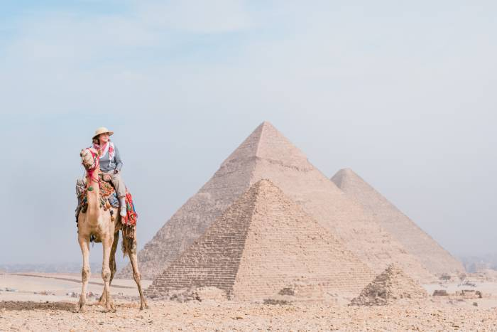 Traveler riding a camel in front of the Great Pyramids of Giza, Egypt.