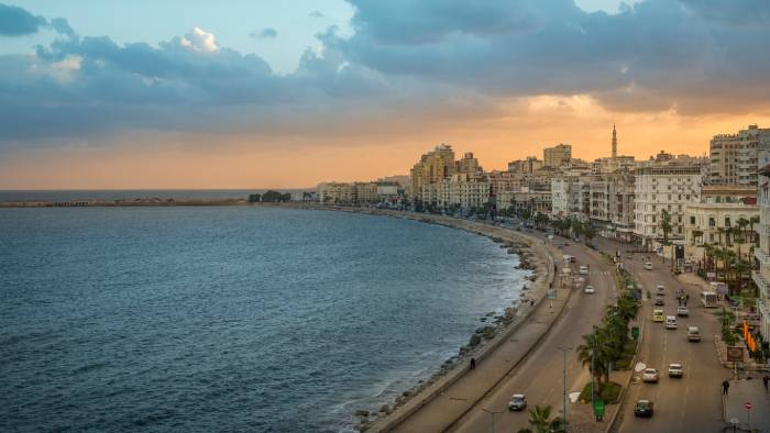 Panoramic view of Alexandria Corniche at sunset with the Mediterranean Sea and the city's iconic waterfront skyline.