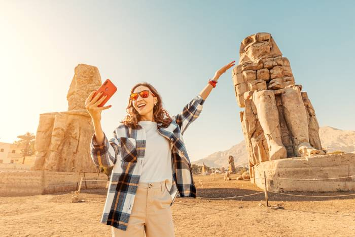 Traveler taking a selfie beside the Colossi of Memnon in Luxor, Egypt.