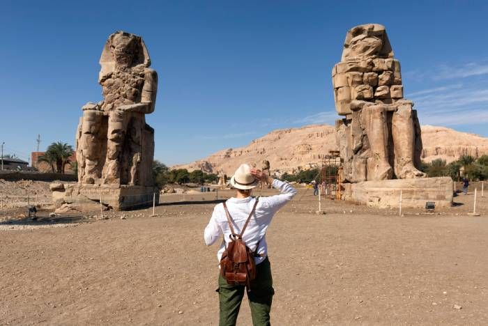 Traveler photographing the Colossi of Memnon in Luxor, Egypt, during a sightseeing tour.