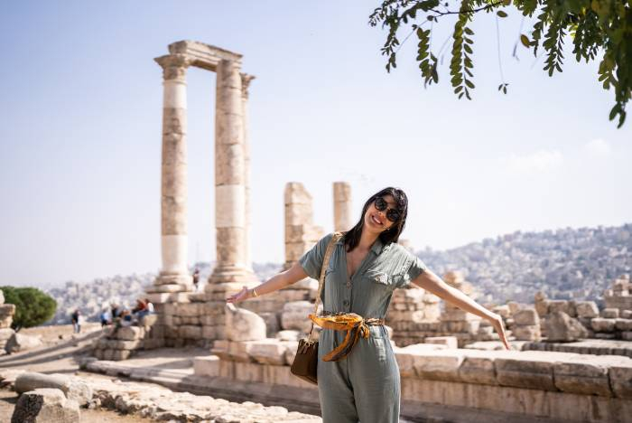 Traveler posing among the ancient Roman ruins of the Amman Citadel with the city skyline in the background, Jordan.