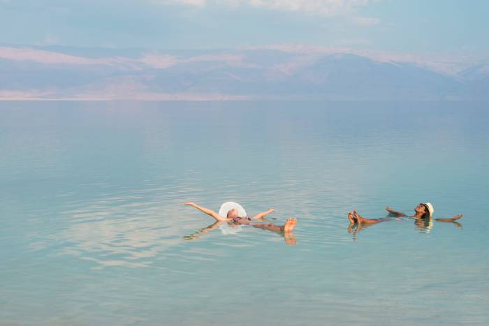 Two travelers floating effortlessly in the Dead Sea with mountains in the background, Jordan.