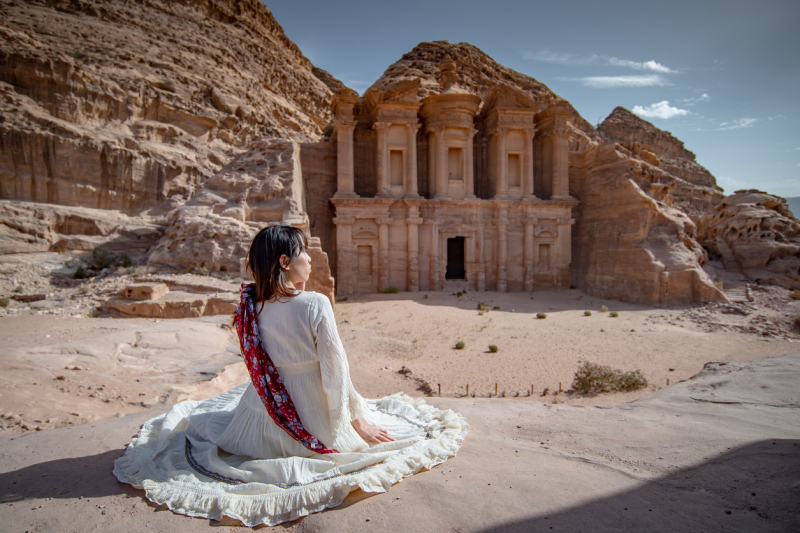 Traveler in a white dress admiring the Monastery (Ad Deir) in Petra, Jordan.