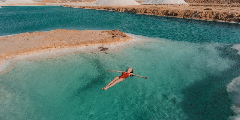 Oasis de Siwa Mujer flotando en aguas turquesas de un lago salado en el Oasis de Siwa, Egipto, rodeada de formaciones desérticas y paisajes áridos.